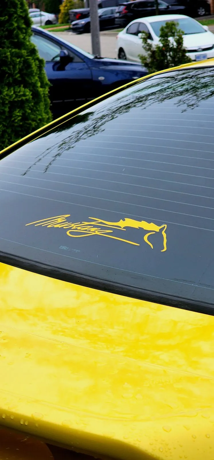 Gold running horse decal on the rear window of a yellow Mustang